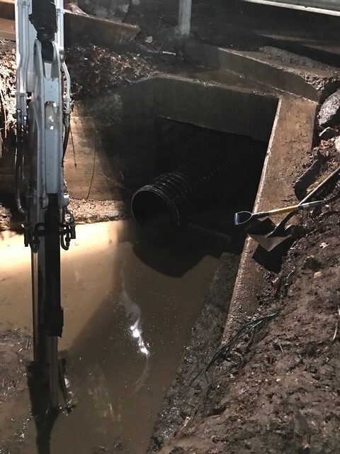 Excavator near muddy water drainage area.