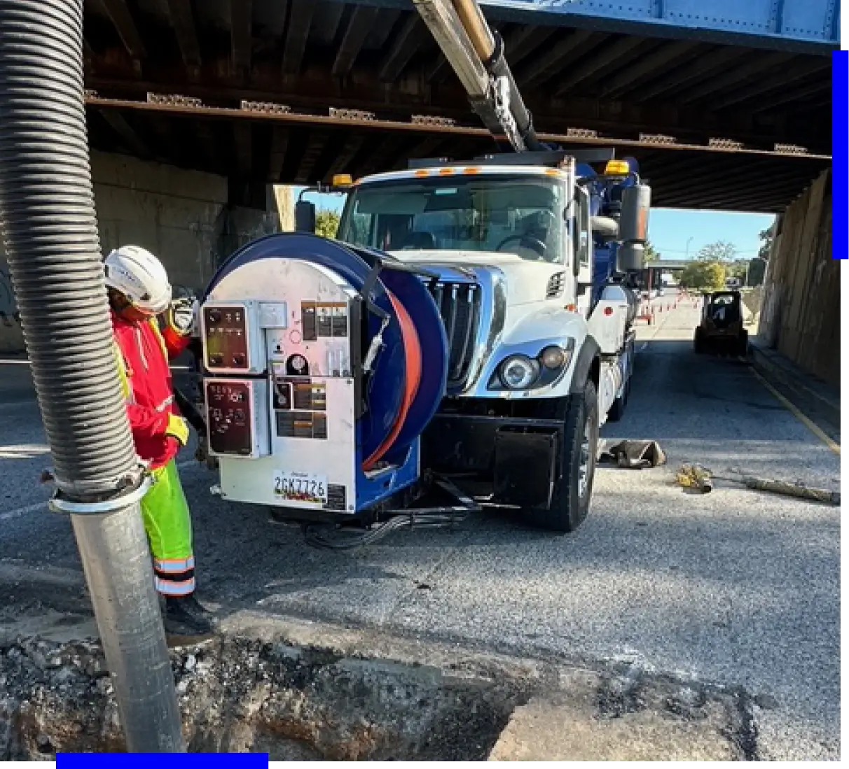 Truck cleaning under bridge with worker nearby.